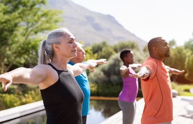 A group of people practising yoga next to a swimming pool in a green, hilly landscape.