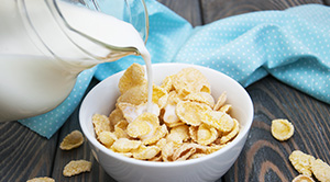 A jug of milk being poured over cereal.