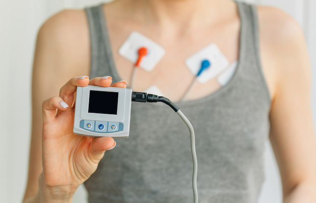 A woman wearing and holding a Holter monitor.