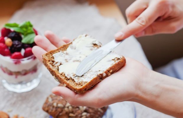 Close up of a person spreading margarine on some seeded bread.
