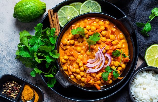 Arial view of a colourful South Asian curry with chickpeas, coriander and wedges of lime.