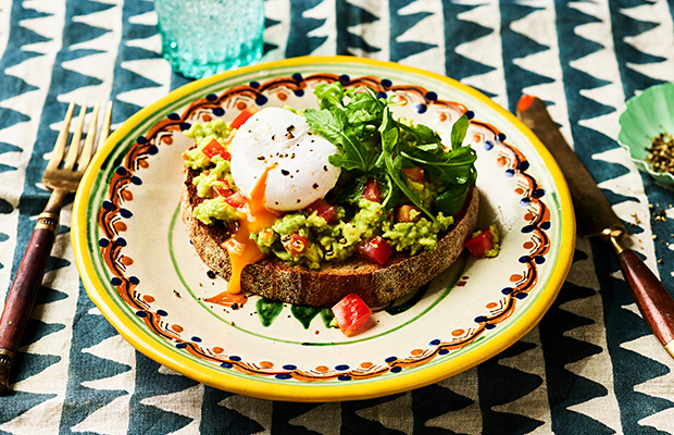 A table with a plate with smashed avocado and a poached egg on toast.