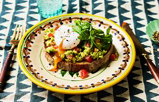 A table with a plate with smashed avocado and a poached egg on toast.