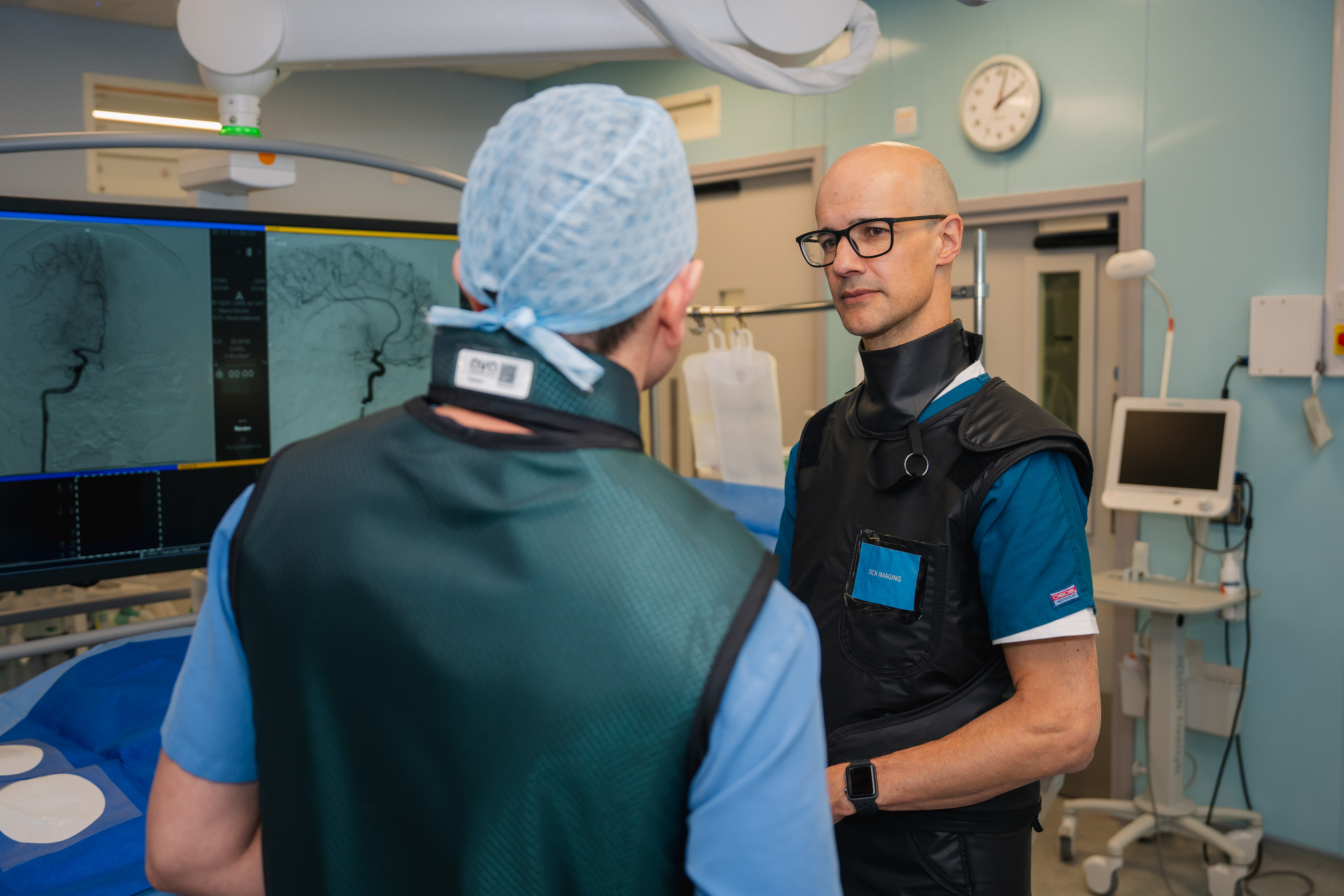 Stroke expert Professor Rustam Al-Shahi Salman with technician Nicholas Dobbs in the angio suite of the University of Edinburgh Imaging Facility, with an image of a carotid artery in the background.