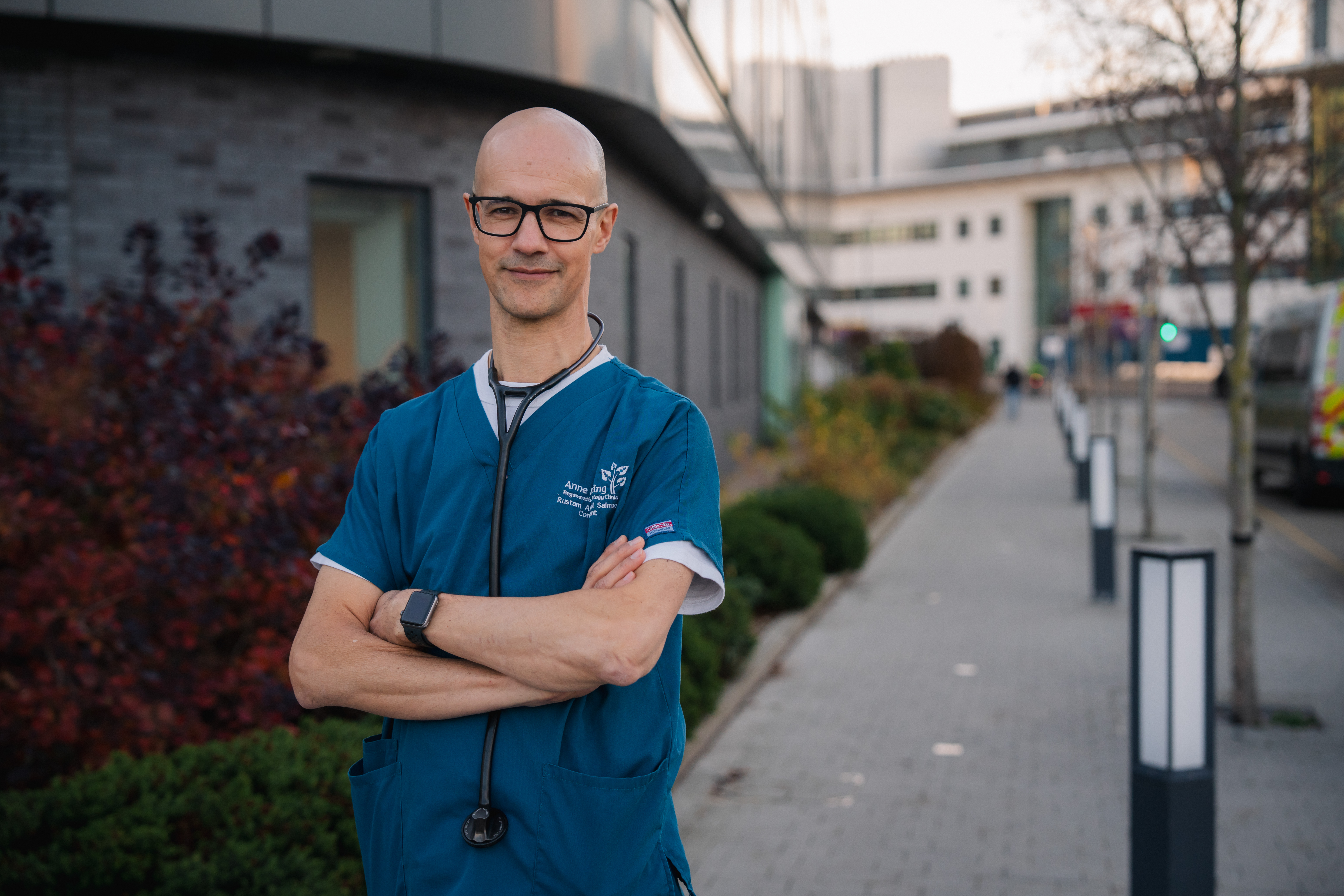 Stroke expert Professor Rustam Al-Shahi Salman in blue scrubs standing outside the University of Edinburgh Imaging Facility.