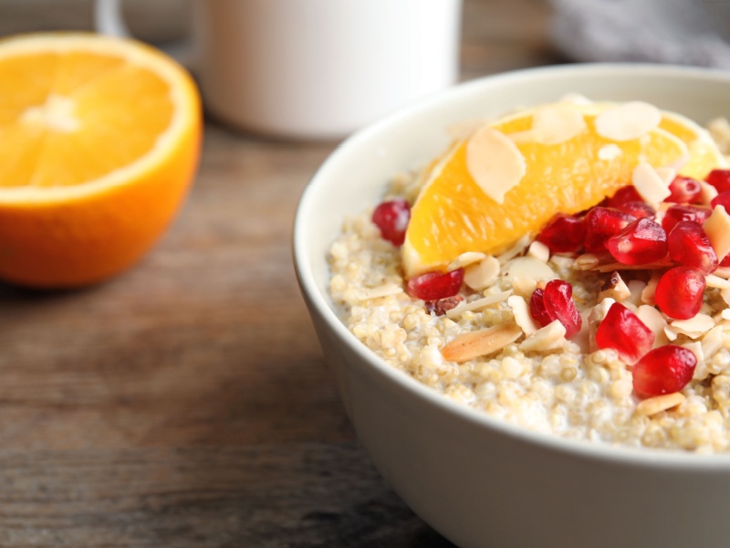 Close up of porridge with orange segments, flaked almonds and promegranate in a white bowl with half an orange in the background.