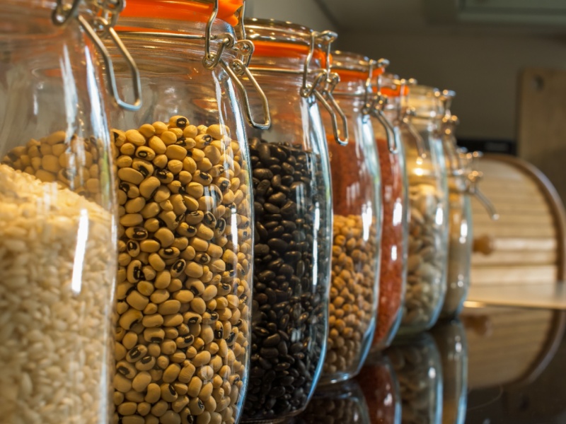 Close up of glass storage jars with various dried pulses and legumes in, on a shelf.