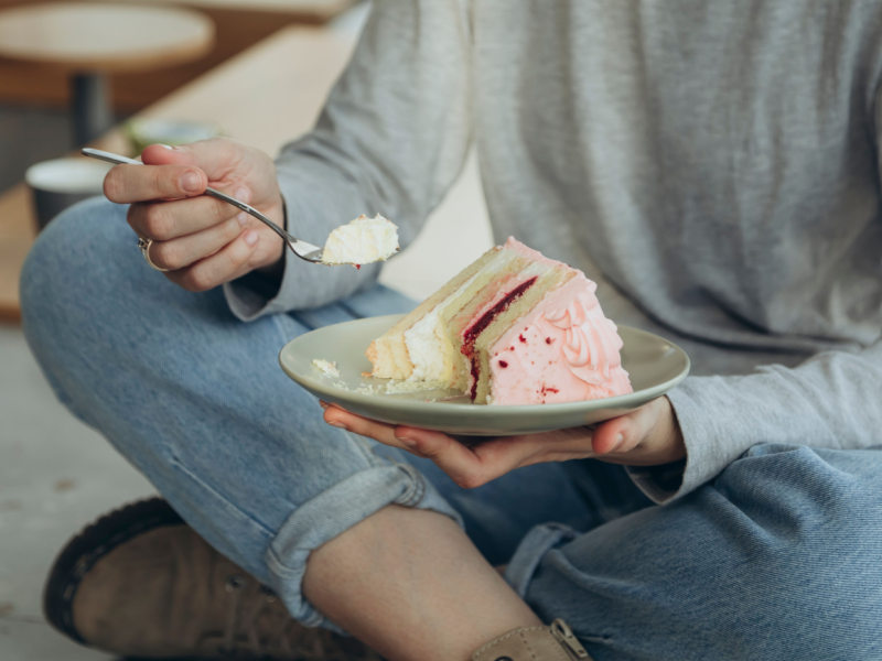 Person sitting cross-legged eating a vegan cake with pink icing with a spoon.