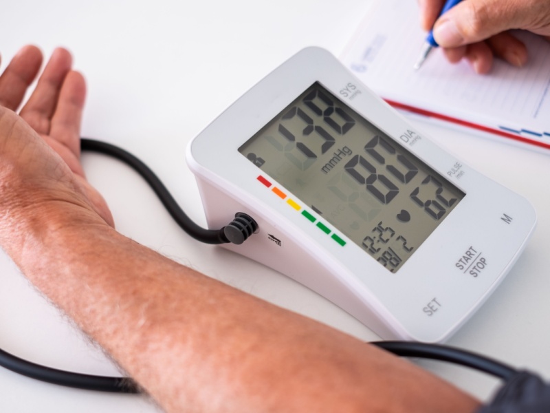 Someone checking their blood pressure with a monitor and writing down the reading.