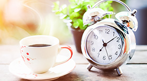 A cup of coffee next to an alarm clock.