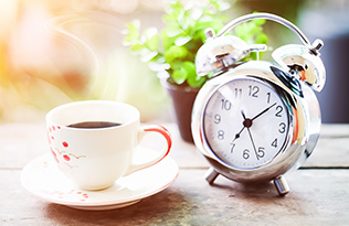 A cup of coffee next to an alarm clock.