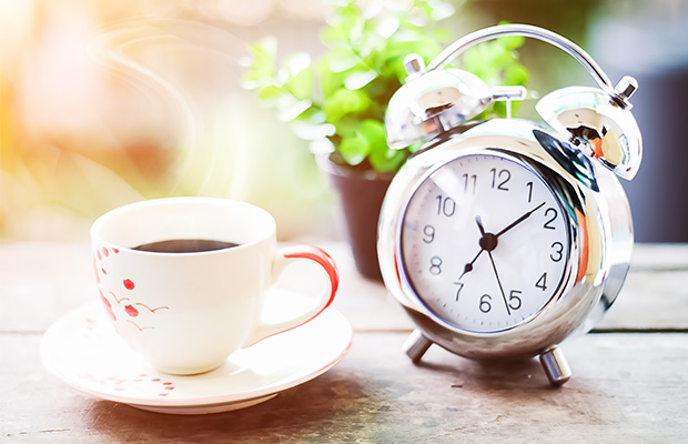 A cup of coffee next to an alarm clock.