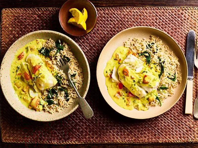 Two bowls of fish curry with rice on a table.