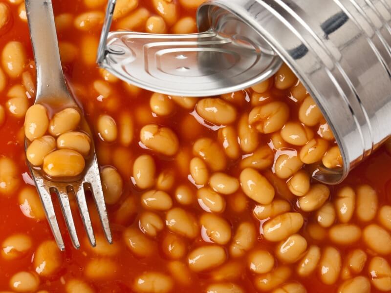 An open tin of baked beans spilling out onto a table with a fork.