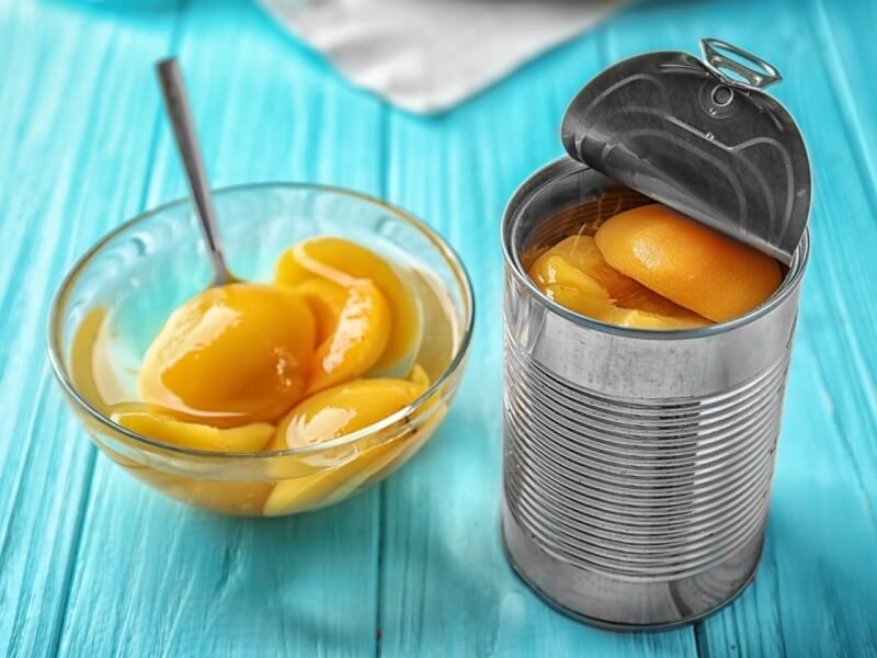 Canned peaches in a glass bowl and in a tin.