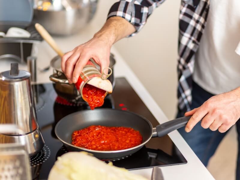 A person pouring a tin of chopped tomatoes into a pan.