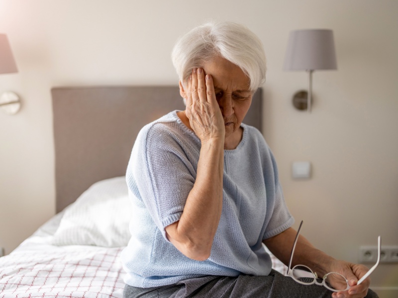 A woman sitting on a bed feeling tired with her head on her face.
