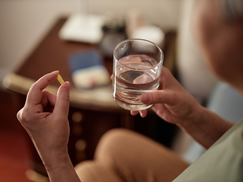 A person holding a pill and a glass of water.