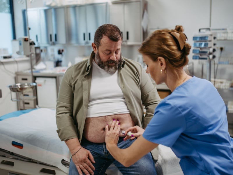 A healthcare professional injecting a man in the stomach.