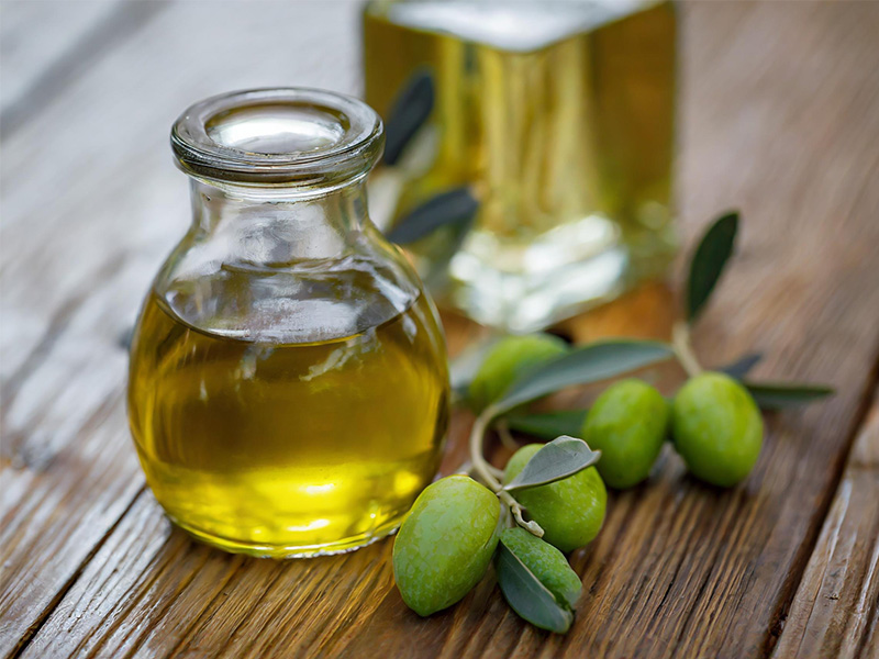 A glass bottle of olive oil next to some olives.