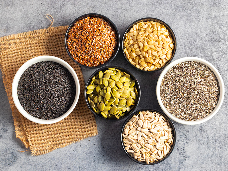 Different types of seeds in small bowls on a table.