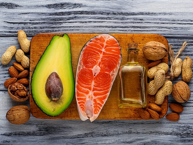 Healthy fatty foods including avocado, salmon , vegetable oil and nuts on a chopping board.