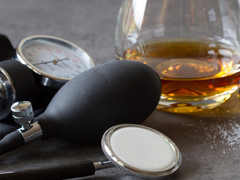 A glass of whiskey next to a blood pressure gauge.