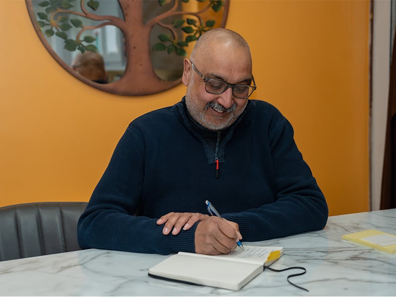 Denis sat at a table writing in a journal.