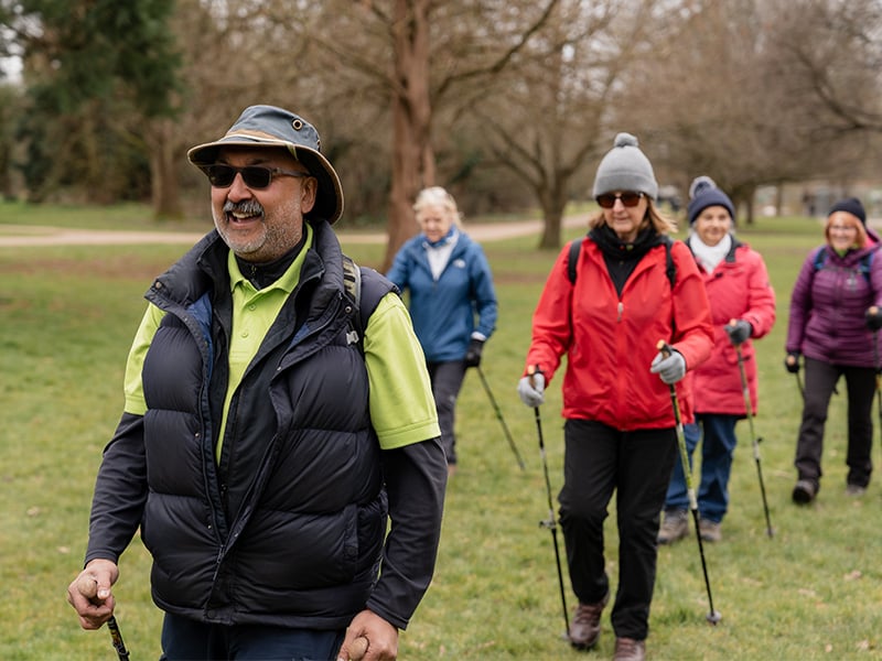 Denis Nordic walking with a group of people in a park.