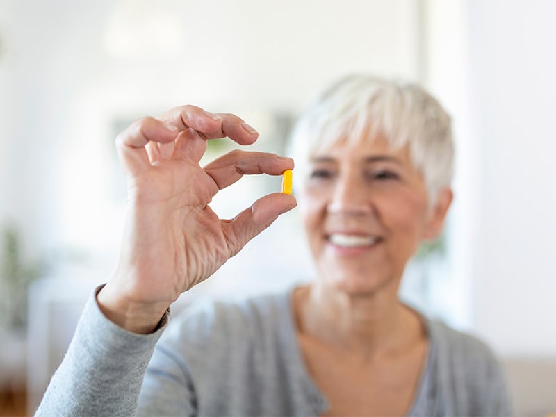 A woman holding up and looking at a pill.