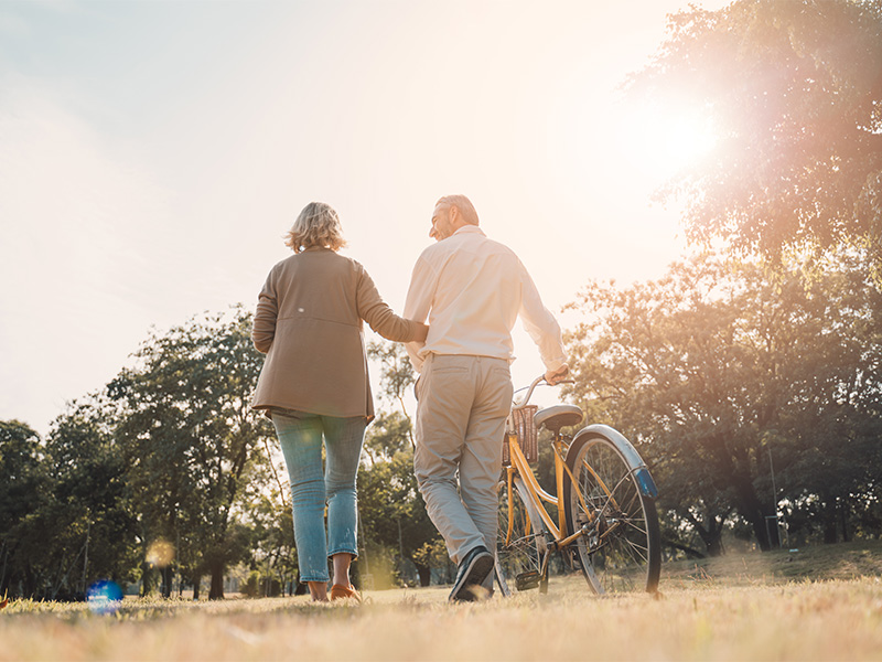 A man and woman walking through a park with a bike.