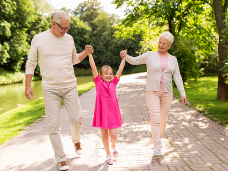 A couple walking with their granddaughter in a park.