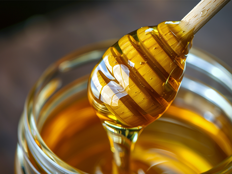 A honey dipper above a jar of honey.