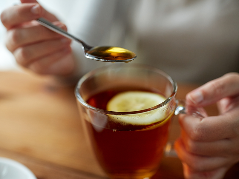 A woman adding a teaspoon of honey to a mug of tea.