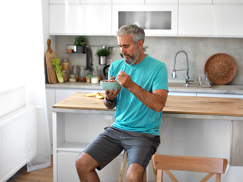 A man in workout gear eating breakfast in a kitchen.