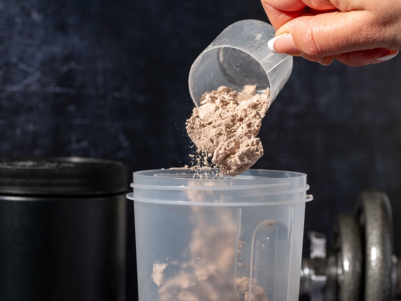 Someone pouring a scoop of protein powder into a cup.