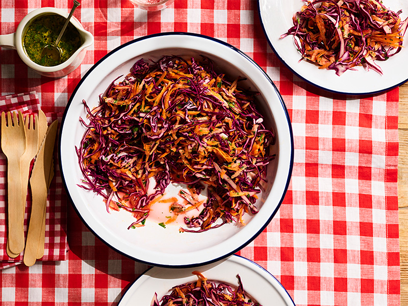 A bowl and plates of red cabbage slaw on a table.