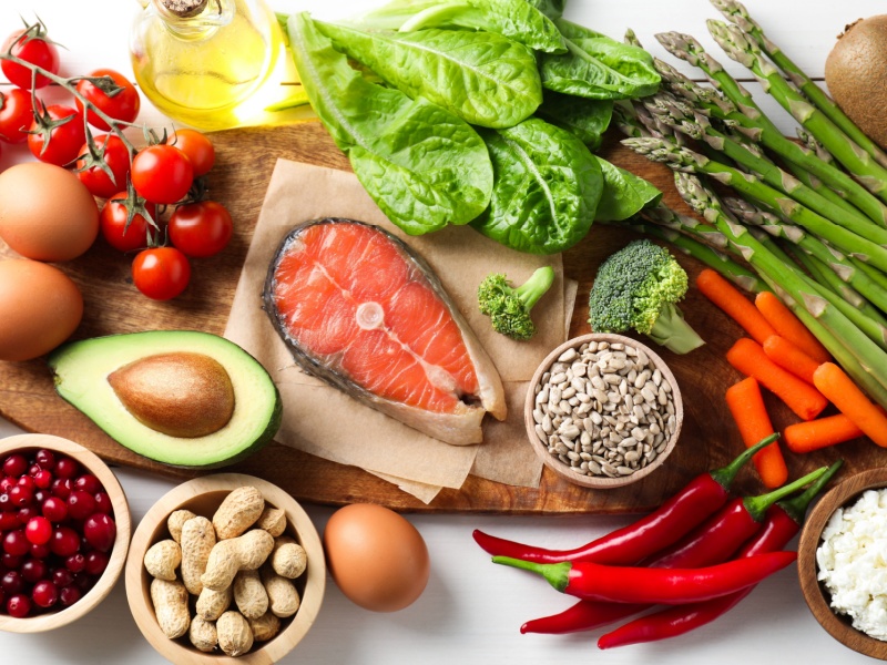 Healthy foods including fruits and vegetables, nuts, seeds and salmon on a table.