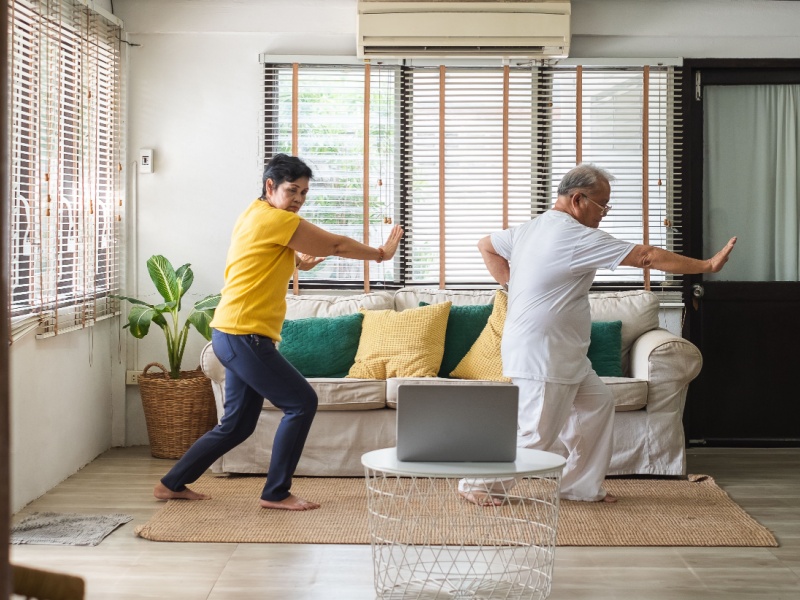 A man and woman practising Tai Chi movements at home in front of a laptop.