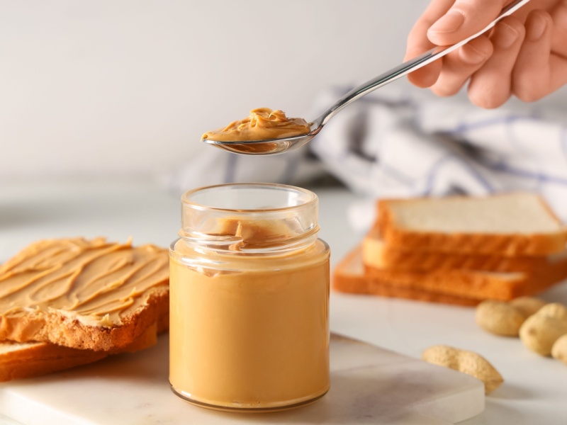 Someone taking a teaspoon of nut butter out of a jar.