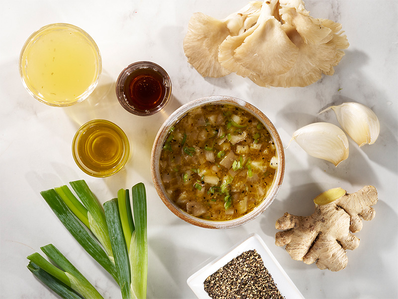 Oyster mushroom and black pepper stir fry sauce in a bowl surrounded by ingredients.