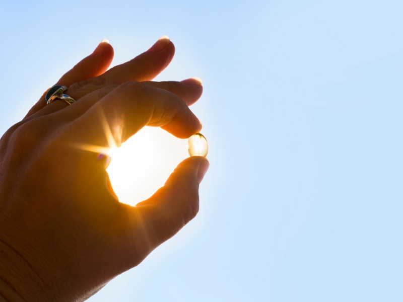 A person holding a vitamin D supplement up towards the sunlight.