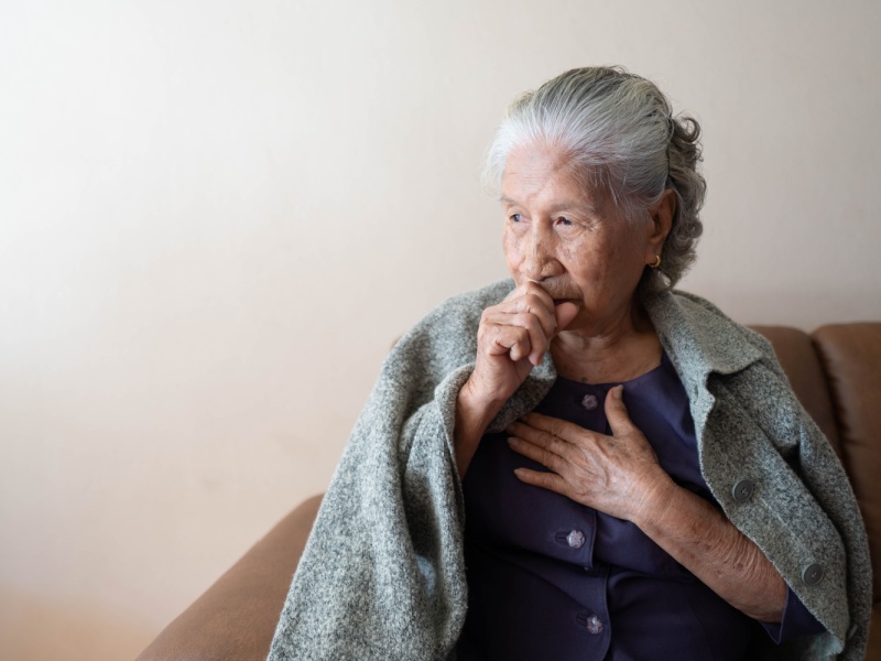 A woman coughing with a blanket over her shoulder.