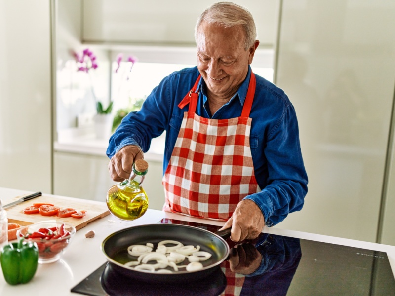 A man frying onions and pouring seed oil over them.