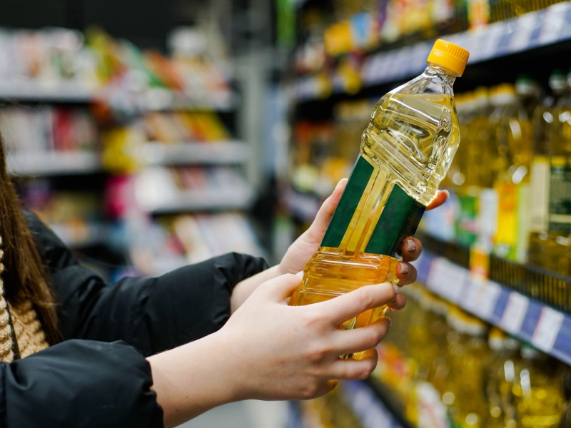 A person reading the label of a bottle of seed oil in a supermarket.