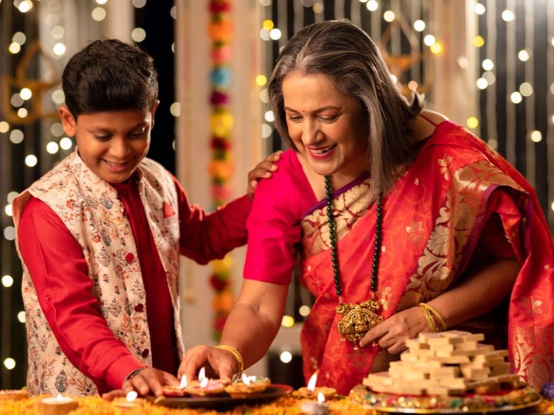 Happy grandmother with grandson lighting diyas in illuminated and decorated home during Diwali celebration.