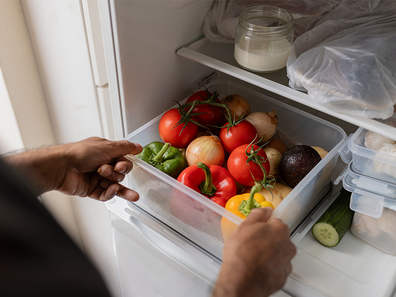Amir pulling fresh vegetables out of his fridge.