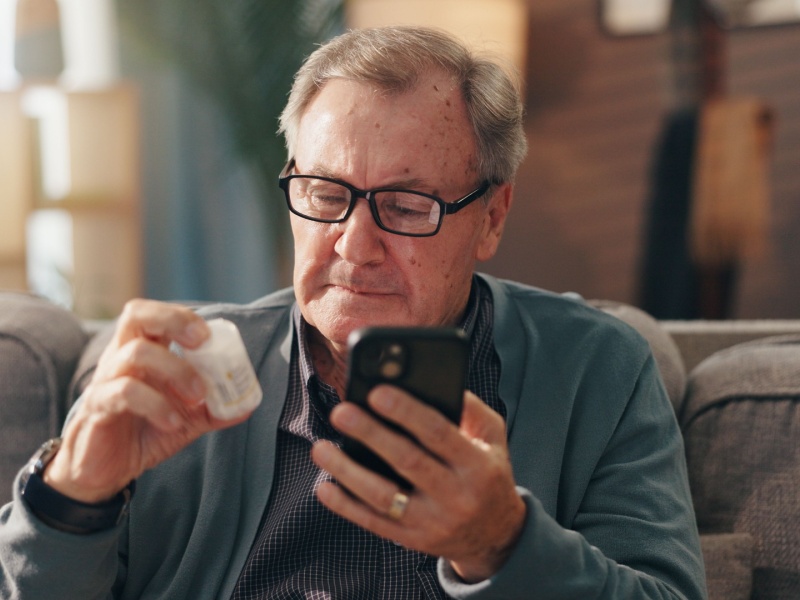 A man reading the label of a bottle of medicine and his holding up his phone.