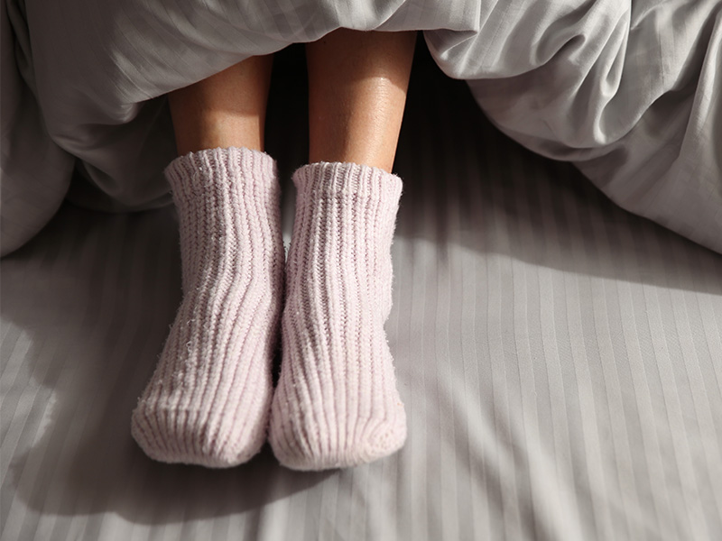 Woman wearing thick pink socks under duvet