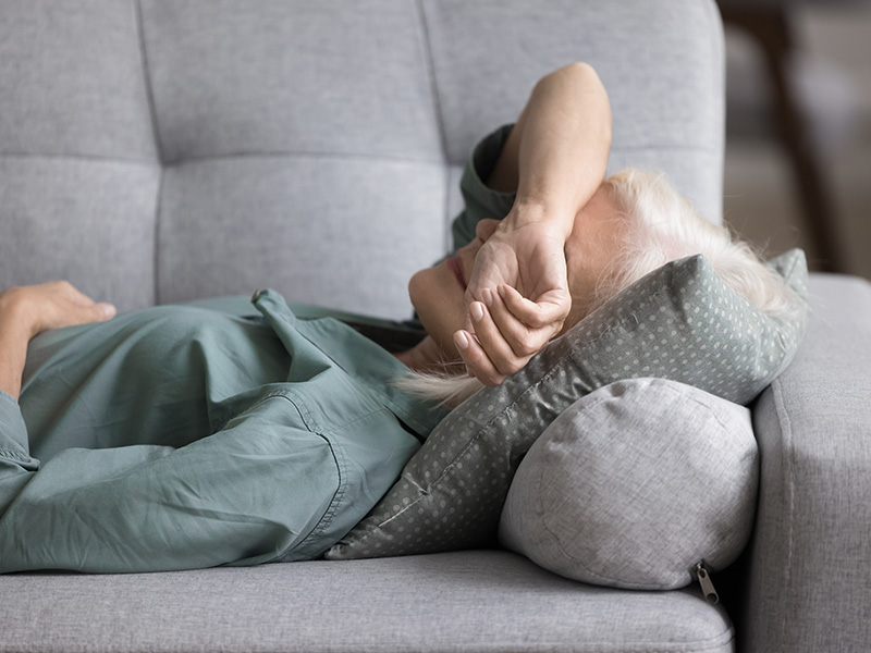 Woman lying on sofa with arm across face tired fatigued